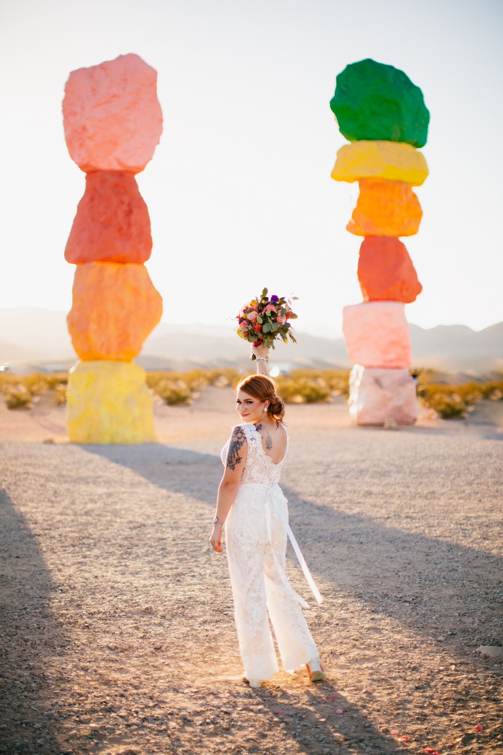 Bride wearing white lace jumpsuit in front of colored rocks.
